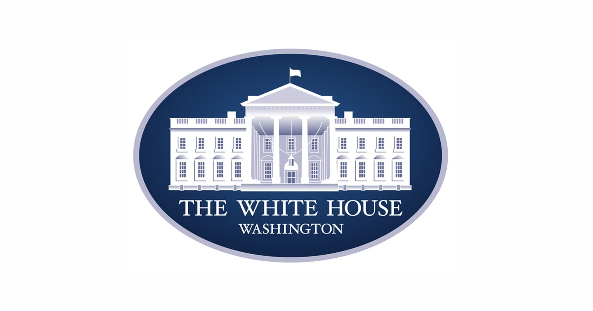 The image shows the official logo of the White House, often seen at events like the Made in America Roundtable. It features a white illustration of the White House on a dark blue oval background, with "THE WHITE HOUSE WASHINGTON" below in capitals.